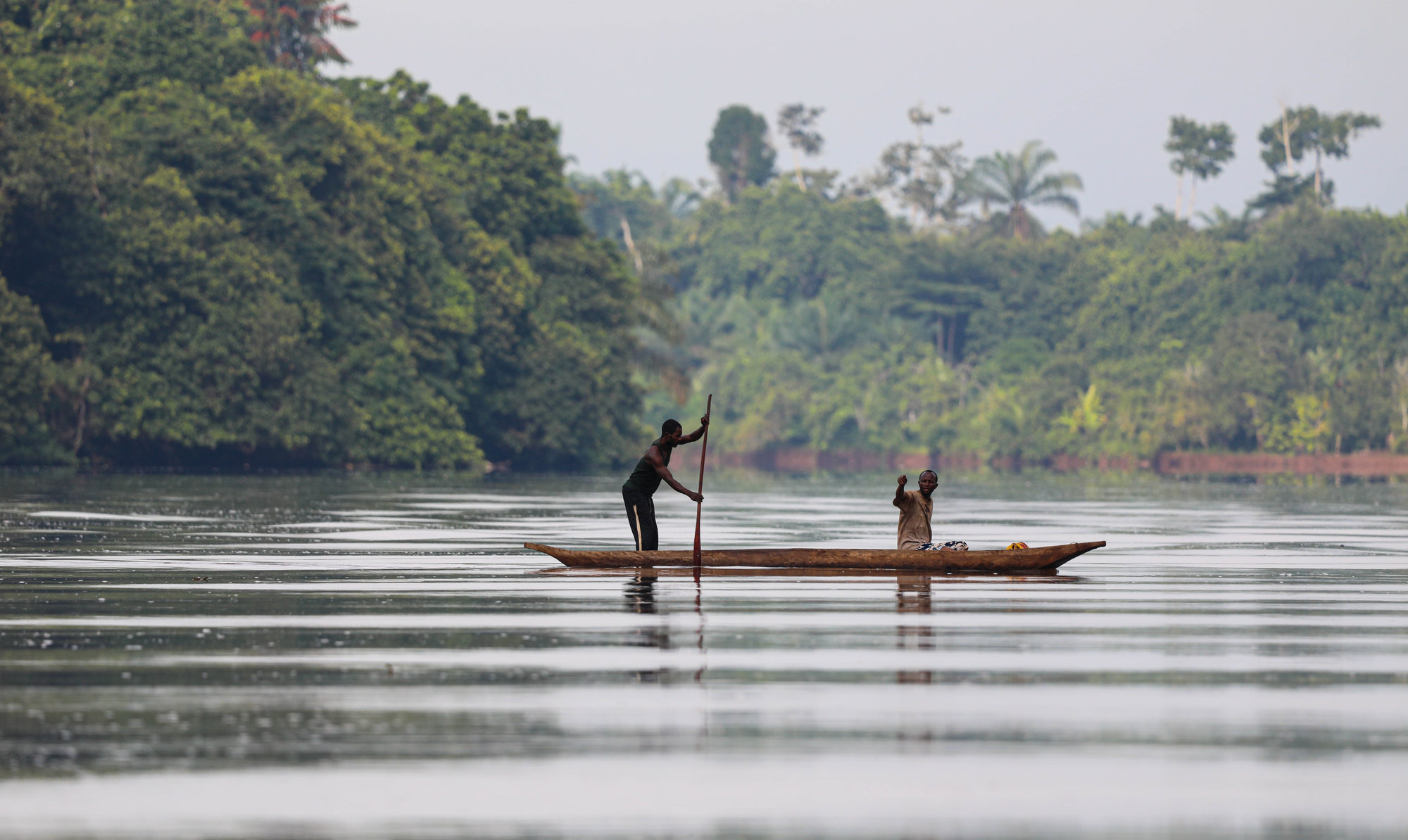 Two men on still water, one rowing standing up